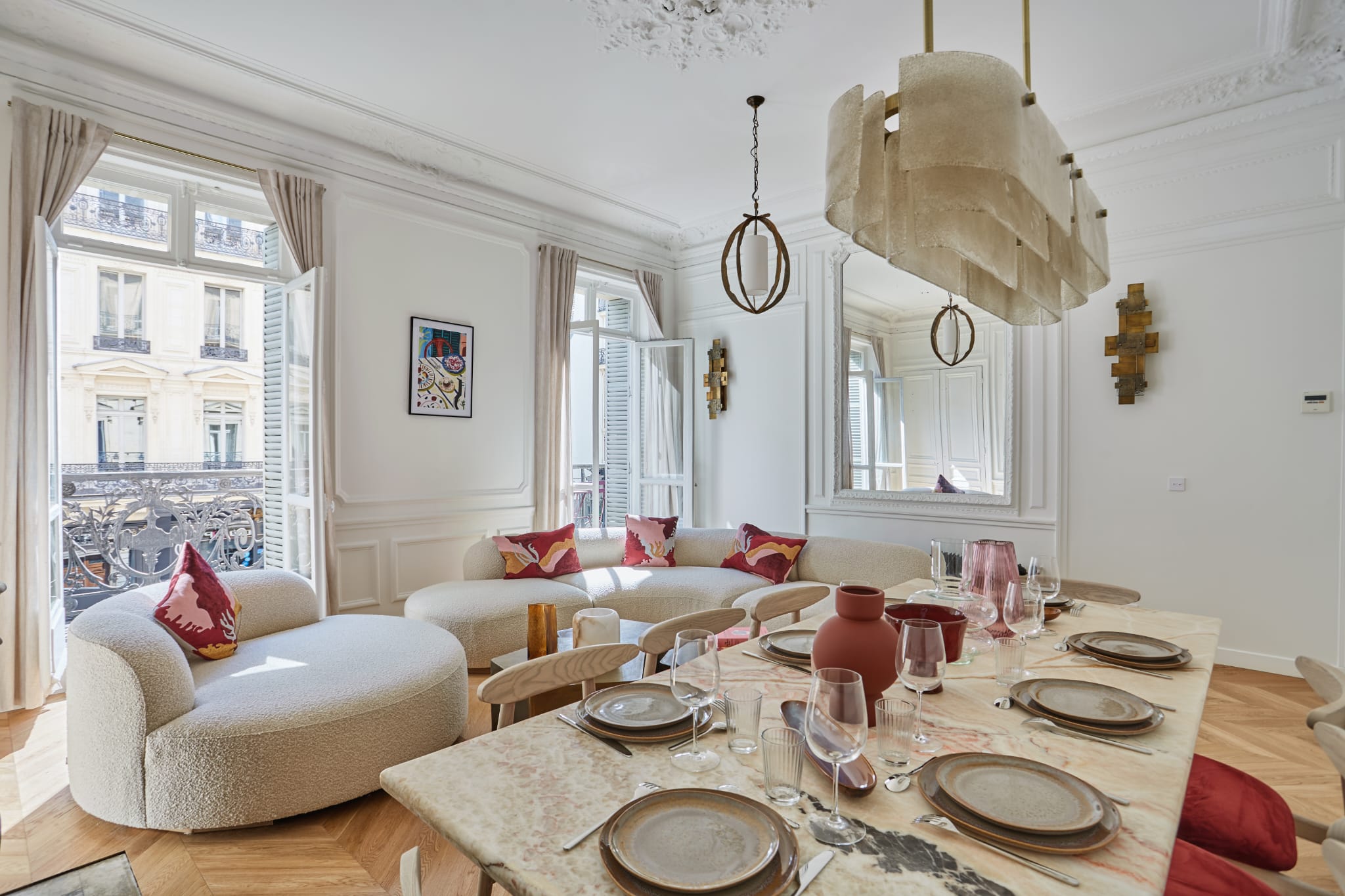 Rénovation complète de maison en île-de-france : devis gratuit 1 Salle à manger lumineuse avec grande table, assises douces et coussins rouges; fenêtres anciennes et décor blanc élégant évoquant une rénovation complète maison île-de-france.